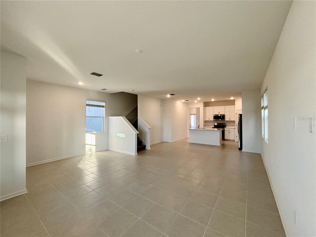 An open-concept living area features light-colored tile flooring, a staircase, and a kitchen with white cabinets — 5770 MEDITATION DRIVE, CLERMONT, FL
