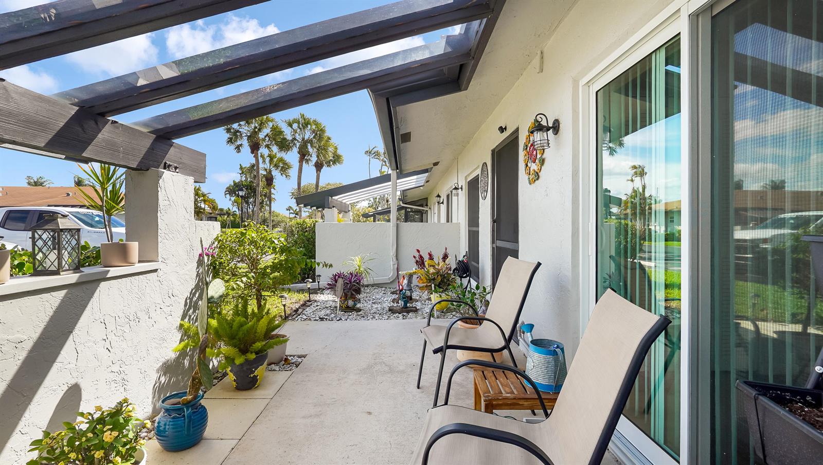 A covered patio features a concrete floor, potted plants, and outdoor seating near sliding doors — 5620 Queen Palm Court # C, Delray Beach FL 33484, DELRAY BEACH, FL