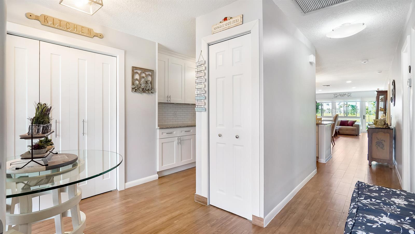 A hallway with light wood flooring leads past a kitchen area toward a living room — 5620 Queen Palm Court # C, Delray Beach FL 33484, DELRAY BEACH, FL