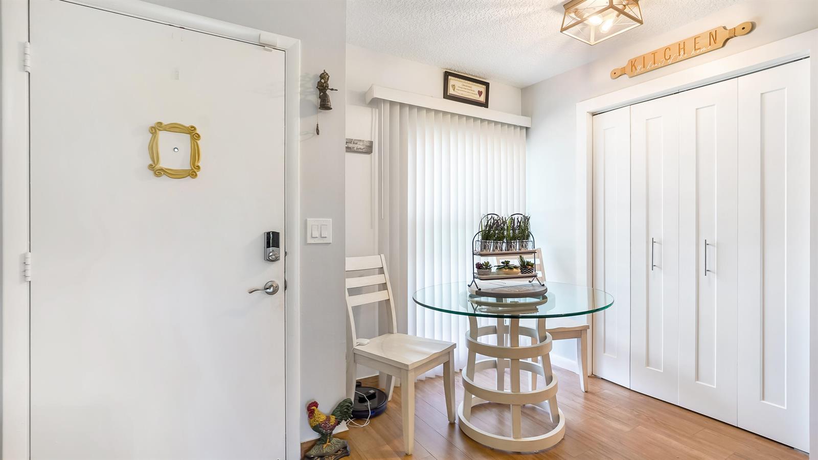 A dining area features a glass-topped table, white chairs, and a door with a yellow frame — 5620 Queen Palm Court # C, Delray Beach FL 33484, DELRAY BEACH, FL