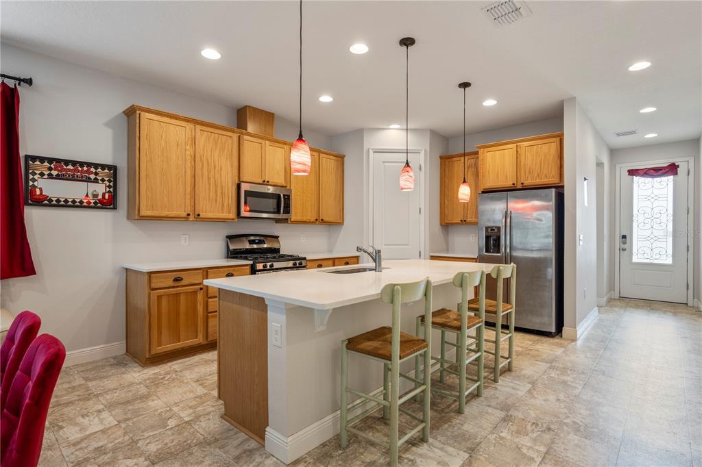 A kitchen features oak cabinets, a white island with bar stools, and stainless steel appliances — 390 CASA VERANO LANE, DAVENPORT, FL