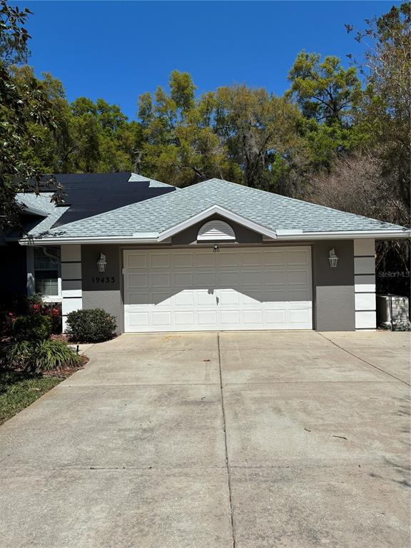 A single-story house with a white garage door, gray siding, and solar panels on the roof — 19433 SW 82ND PLACE ROAD, DUNNELLON, FL