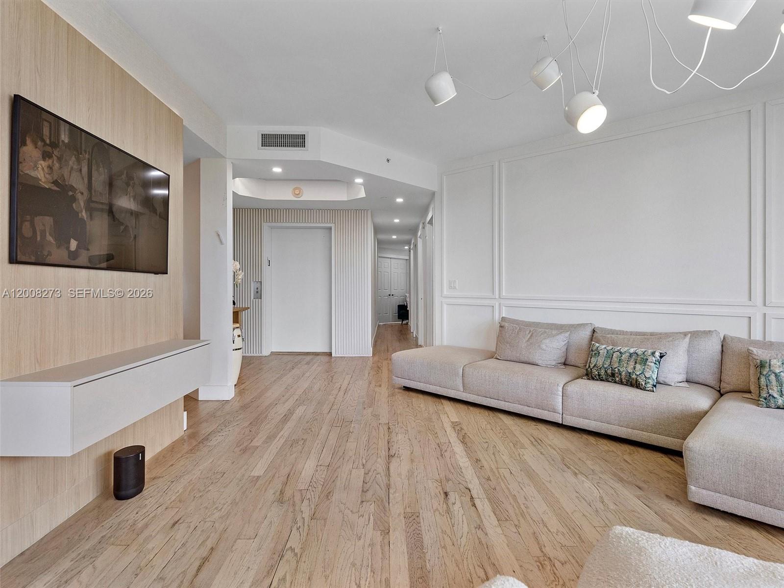 A living room features light wood flooring, a wall-mounted television, and a large sectional sofa — 9751 E Bay Harbor Dr # 11A, Bay Harbor Islands FL 33154, BAY HARBOR ISLANDS, FL