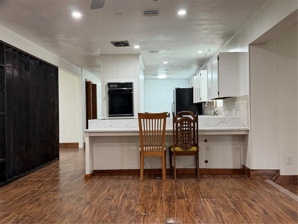 A kitchen features a breakfast bar with two chairs, white cabinetry, and wood-look flooring — 16726 NW COUNTY ROAD 235A, ALACHUA, FL