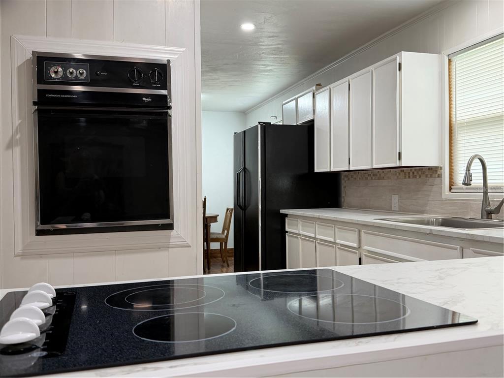 A kitchen features a black wall oven, a black refrigerator, white cabinets, and a cooktop — 16726 NW COUNTY ROAD 235A, ALACHUA, FL