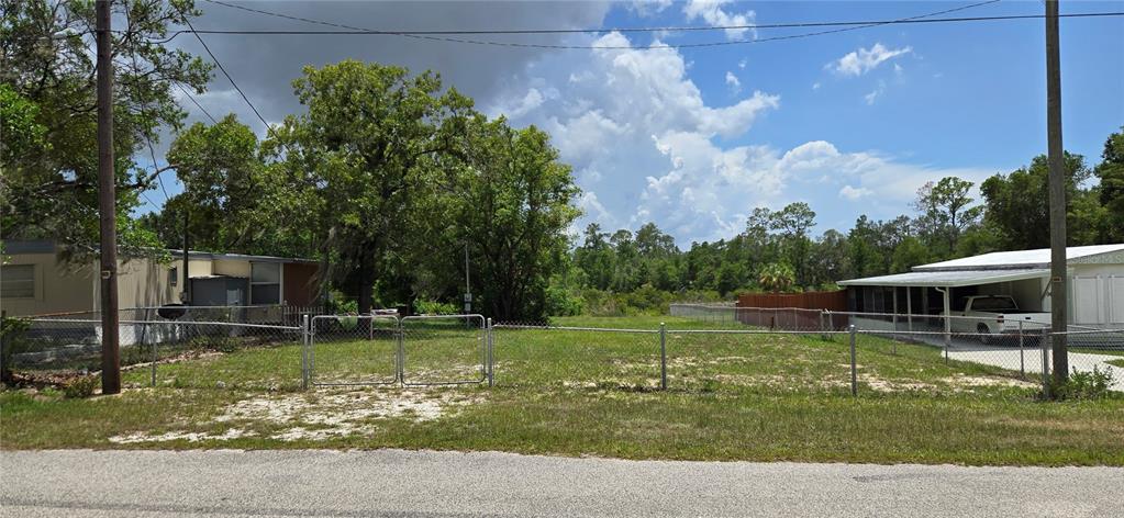 A vacant, fenced residential lot sits between two mobile homes under a cloudy sky — 0 LAKE DRIVE, WEEKI WACHEE, FL