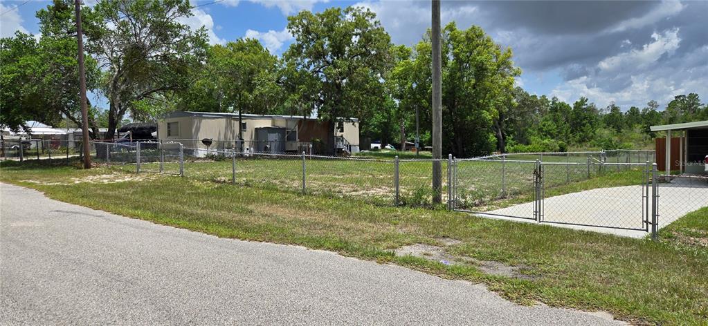 A fenced residential lot features a mobile home, mature trees, and a concrete driveway — 0 LAKE DRIVE, WEEKI WACHEE, FL