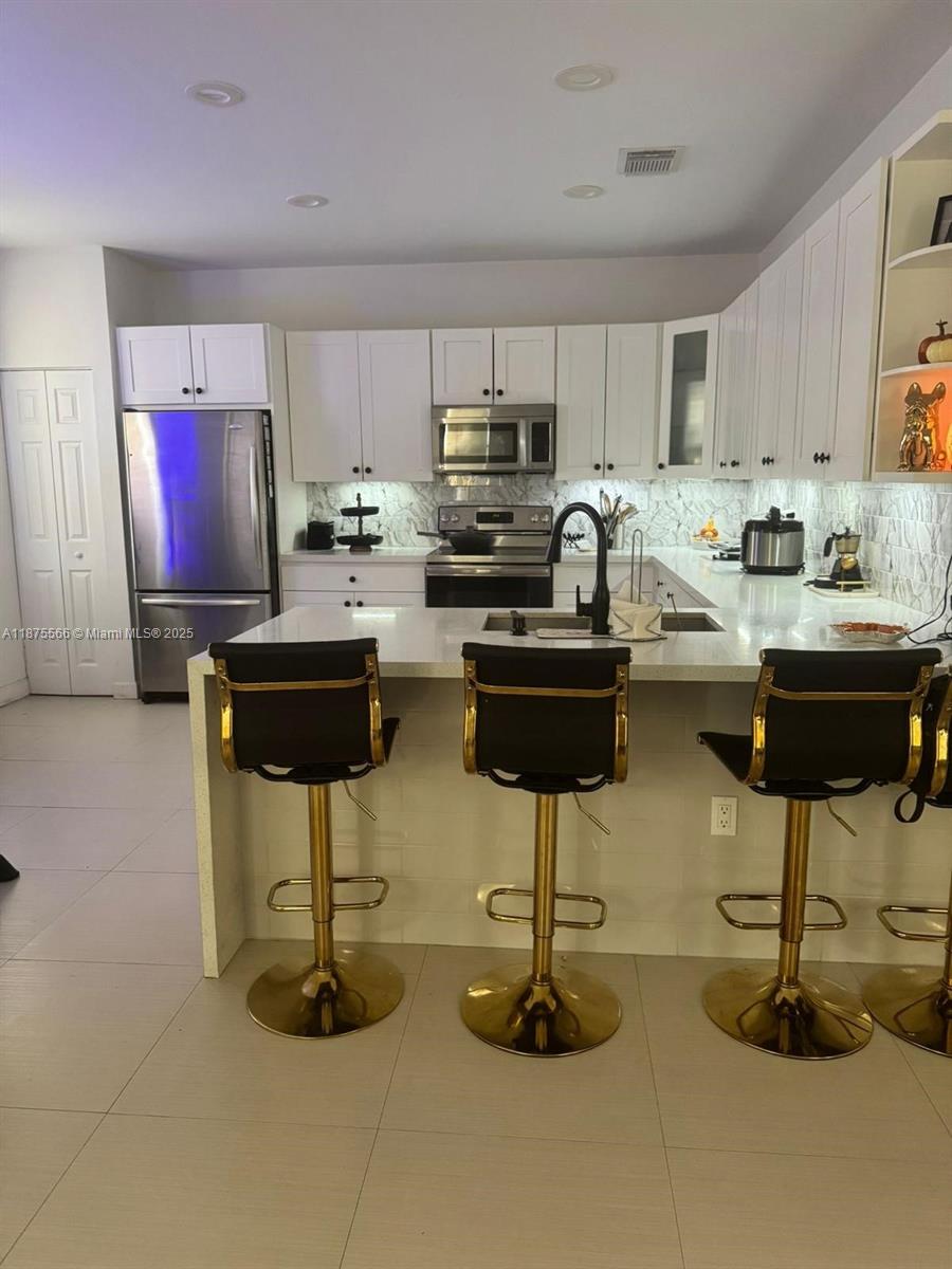 A modern kitchen features white cabinets, stainless steel appliances, and a breakfast bar with stools — 7414 NW 107th Ct, Doral FL 33178, DORAL, FL