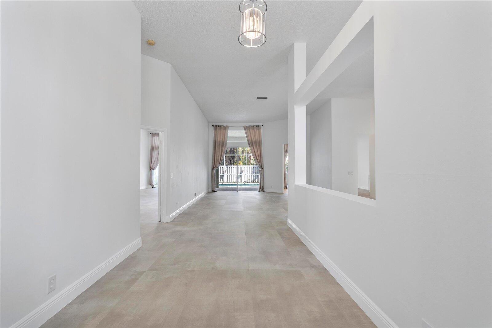 A bright, empty hallway with light-colored tile flooring leads toward a glass sliding door — 970 Greenwood Road, Weston FL 33327, WESTON, FL