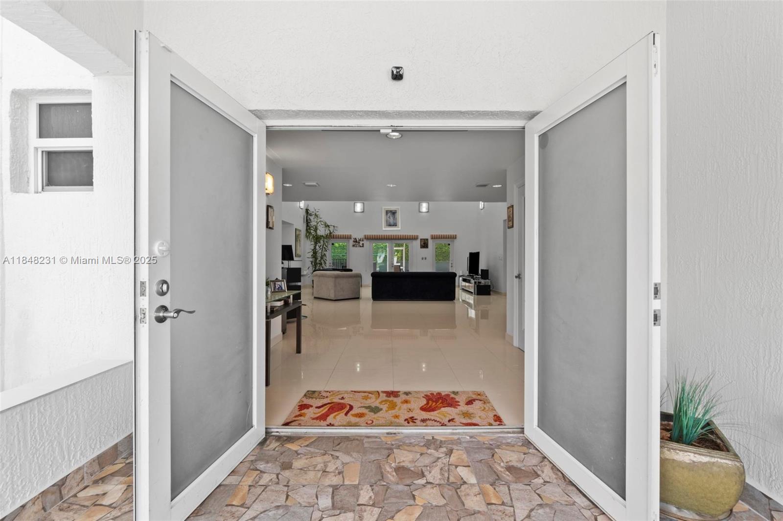 An open double door reveals a spacious living room with light tile floors and furniture — 5045 SW 67th Ave, South Miami FL 33155, SOUTH MIAMI, FL