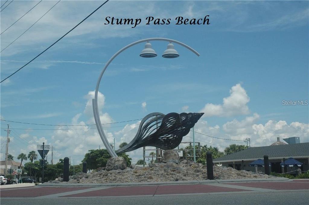 A large metal seashell sculpture sits in the center of a landscaped traffic roundabout — ORTIZ BOULEVARD, NORTH PORT, FL