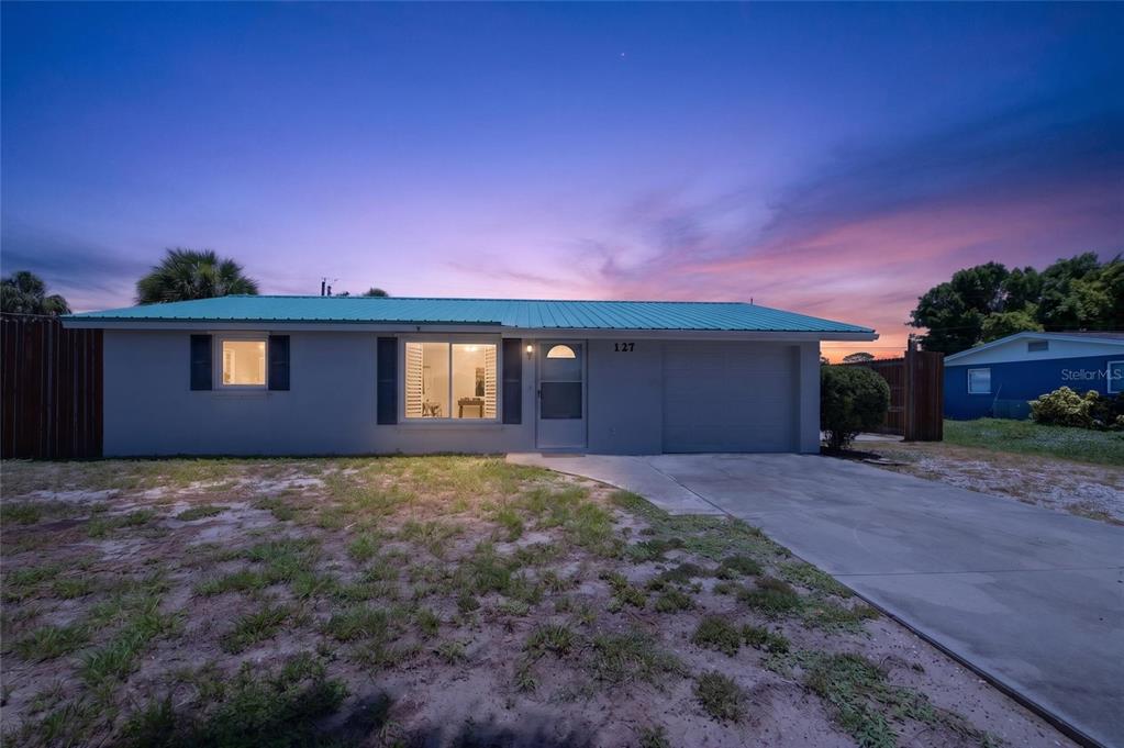 A single-story house with a teal metal roof and a concrete driveway at sunset — 127 COLUMBIA ROAD, VENICE, FL