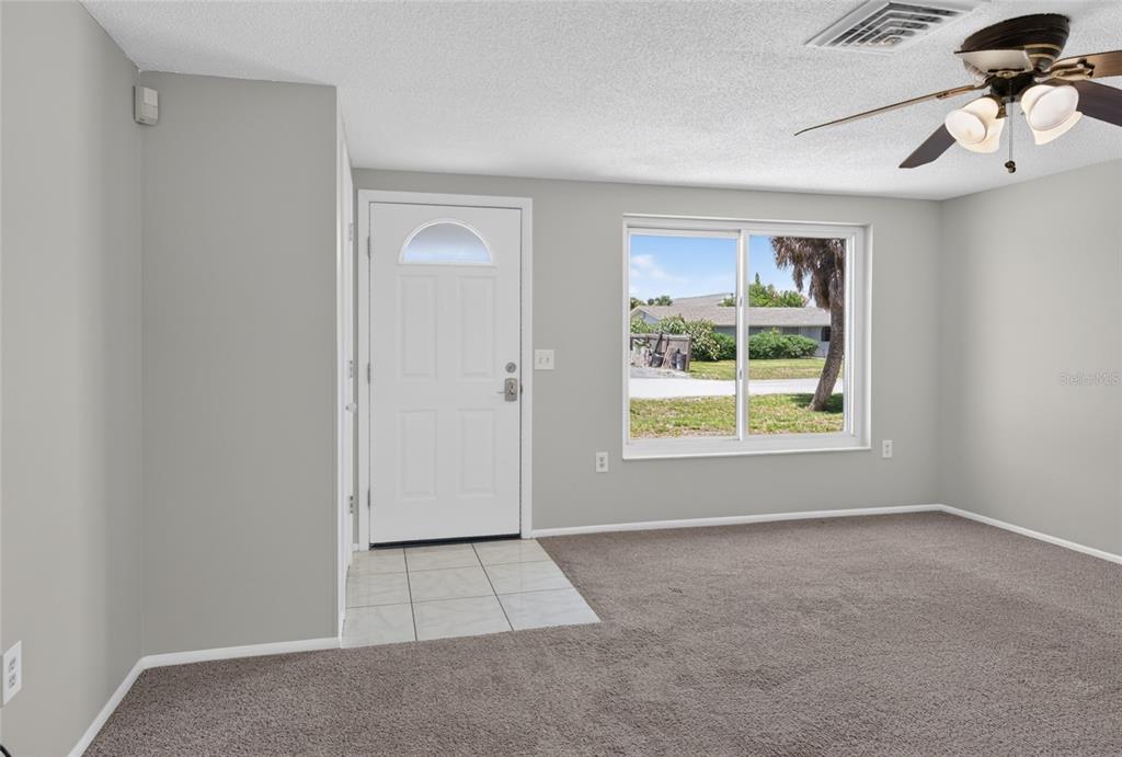A living room features gray walls, brown carpet, a white front door, and a ceiling fan — 127 COLUMBIA ROAD, VENICE, FL