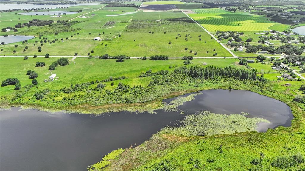 An aerial view shows a large pond surrounded by green fields, trees, and rural properties — 8450 ALTURAS BABSON PARK CUTOFF ROAD, BARTOW, FL