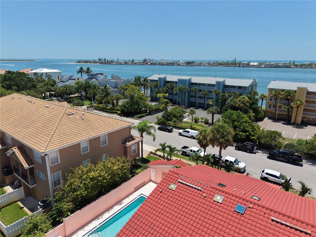 An aerial view shows a swimming pool, residential buildings, a street, and a coastal waterway — 357 8TH AVENUE N UNIT 4, TIERRA VERDE, FL