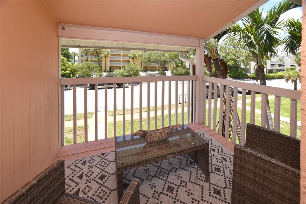 A covered balcony features wicker furniture, a patterned rug, and a view of the parking lot — 357 8TH AVENUE N UNIT 4, TIERRA VERDE, FL