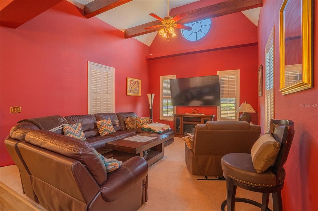 A living room with red walls, a vaulted ceiling with beams, and a leather sectional — 1415 PIER COURT, LAKELAND, FL