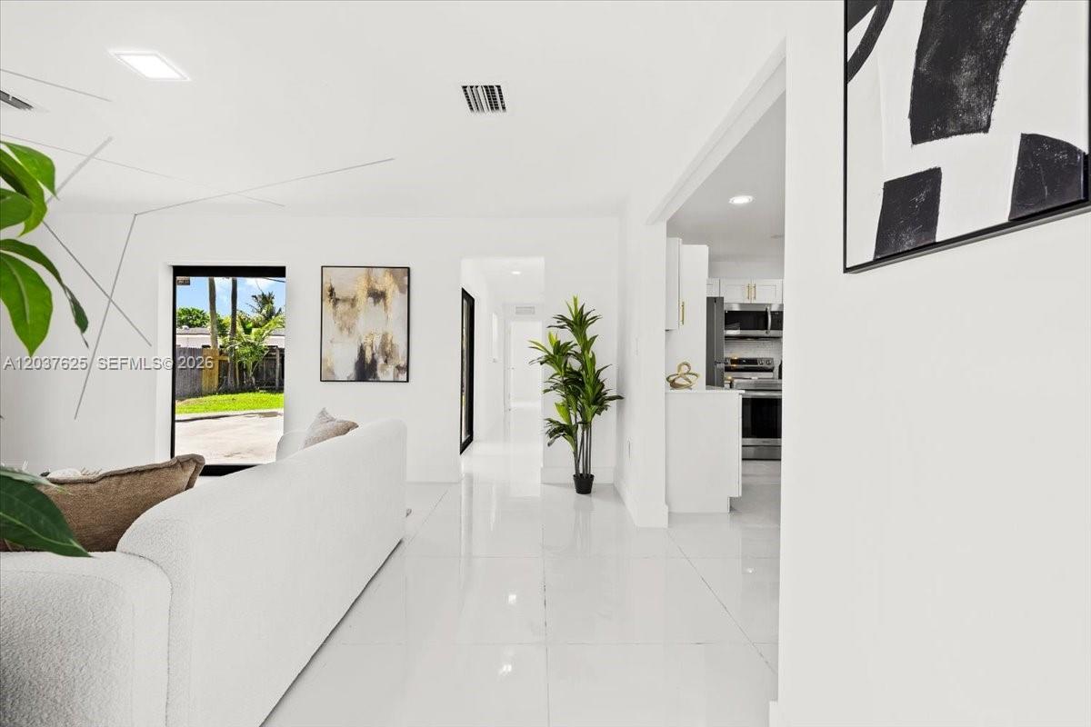A bright living room features white tile floors, a white sofa, and a view into the kitchen — 7500 Venetian St, Miramar FL 33023, MIRAMAR, FL