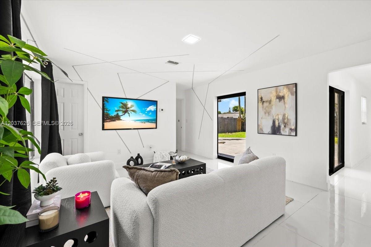 A modern living room features white walls with geometric lines, white furniture, and tile flooring — 7500 Venetian St, Miramar FL 33023, MIRAMAR, FL