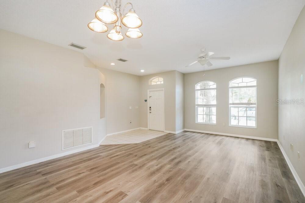 An empty living room features light-colored walls, wood-look flooring, a ceiling fan, and arched windows — 5310 BRADDOCK DRIVE, ZEPHYRHILLS, FL