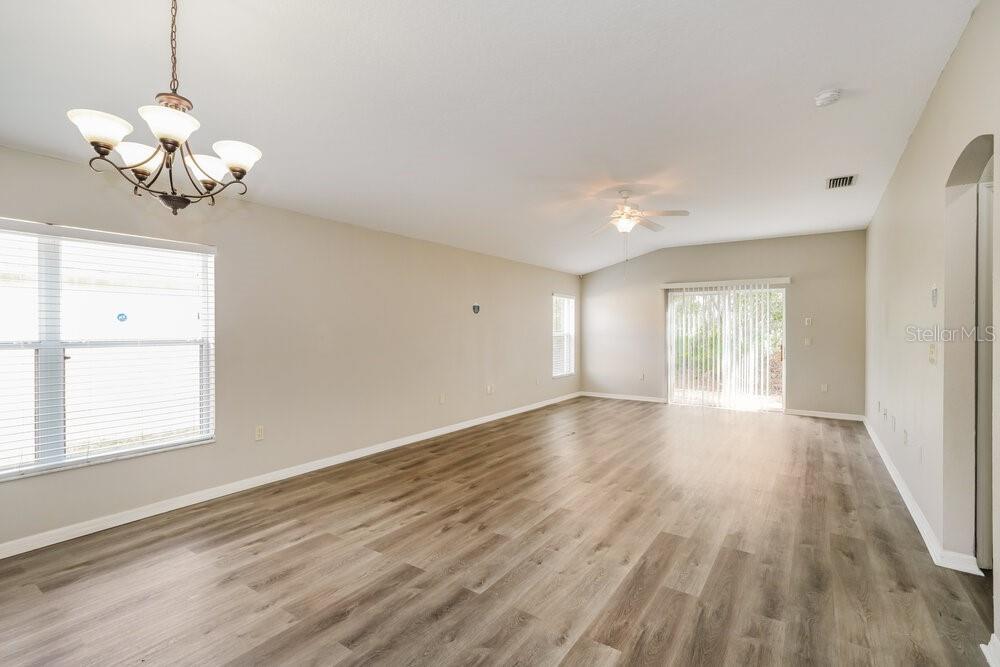 An empty living room features light-colored walls, wood-look flooring, a ceiling fan, and a chandelier — 5310 BRADDOCK DRIVE, ZEPHYRHILLS, FL