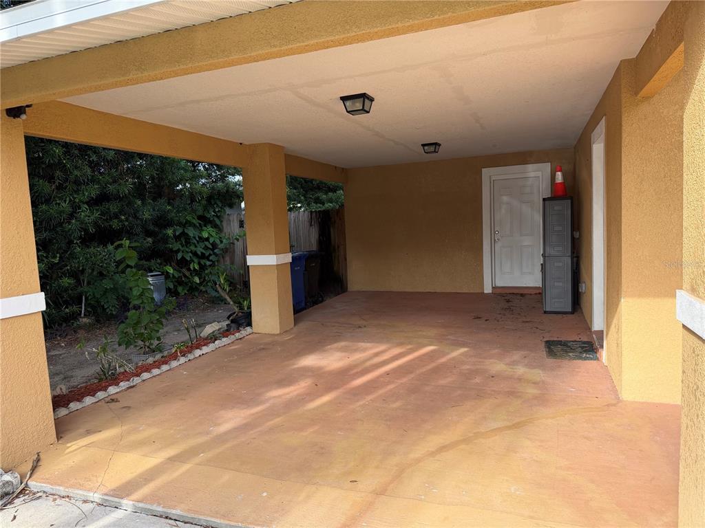 A covered carport with a concrete floor, two ceiling lights, and a white entry door — 1131 DOGWOOD AVENUE, TAMPA, FL