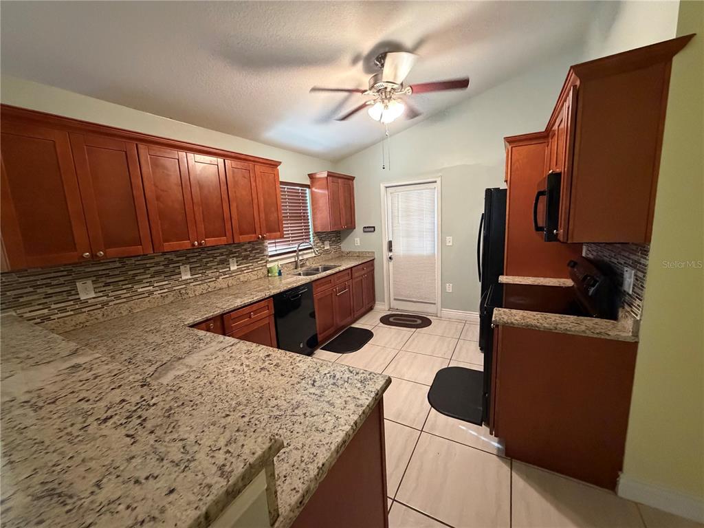 A kitchen features wood cabinets, granite countertops, a tiled backsplash, and black appliances — 1131 DOGWOOD AVENUE, TAMPA, FL
