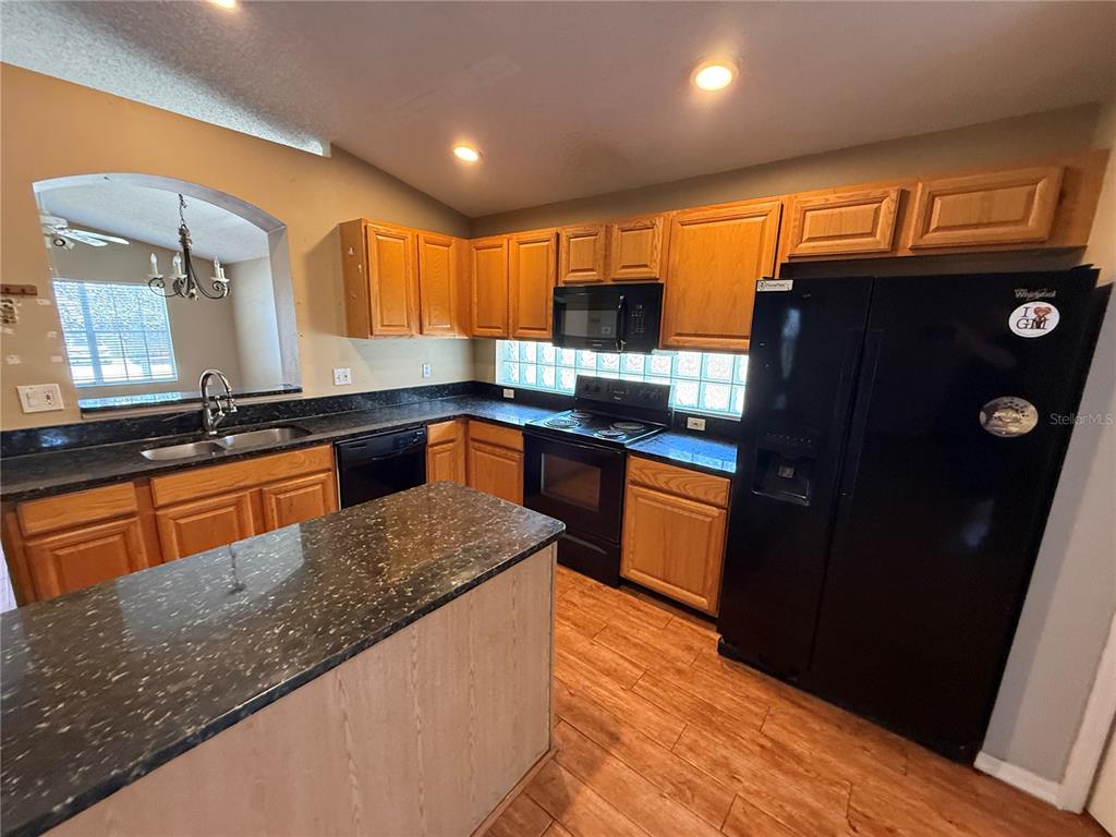 A kitchen features oak cabinets, black appliances, a dark granite island, and glass block windows — 10536 RODONDO DRIVE, ORLANDO, FL