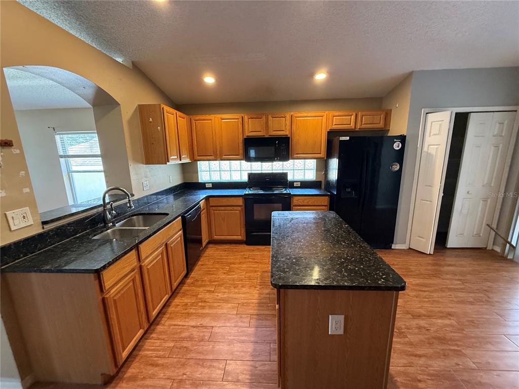 A kitchen features wood cabinets, dark countertops, a central island, and black appliances — 10536 RODONDO DRIVE, ORLANDO, FL