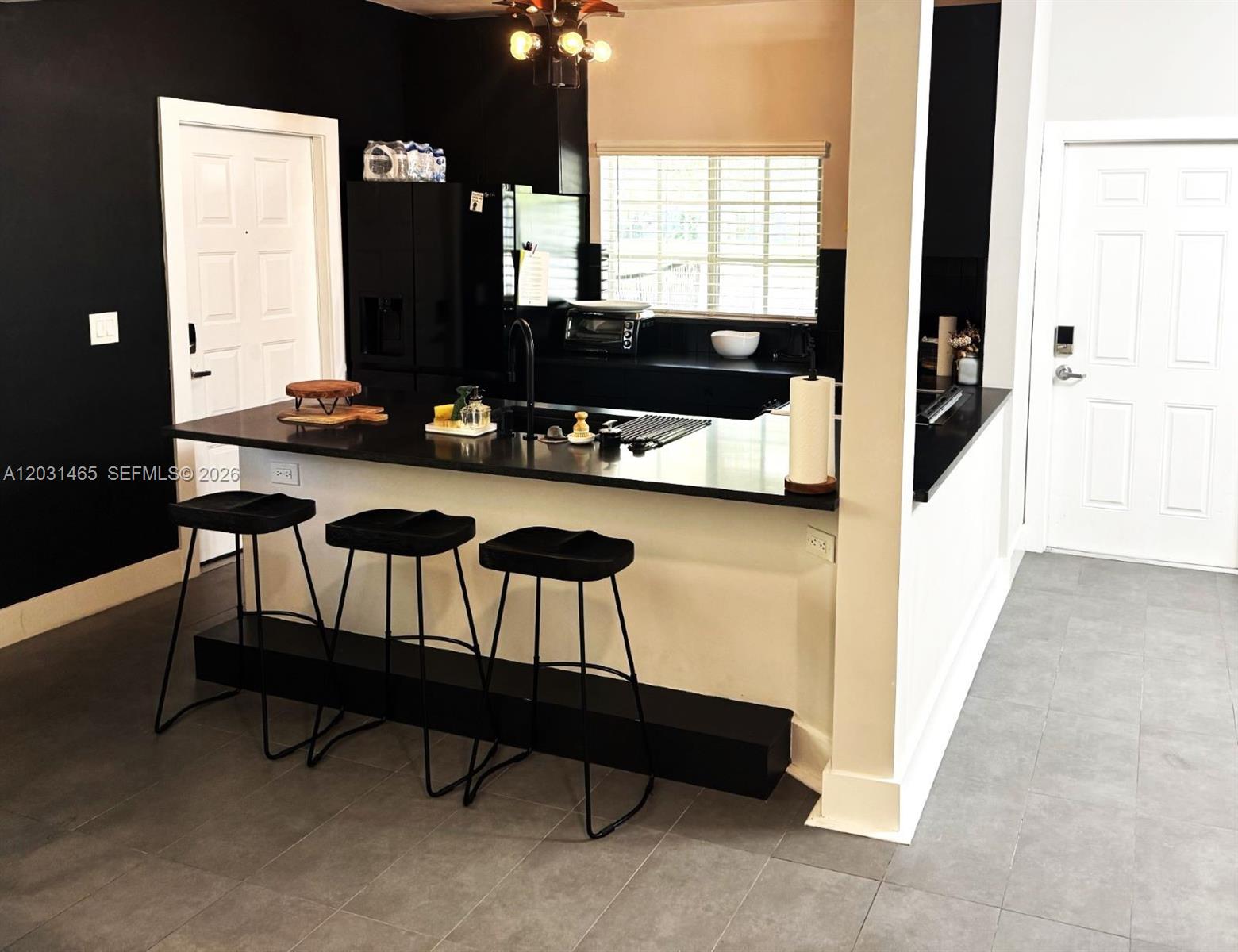 A modern kitchen features black cabinets, a breakfast bar with three stools, and tiled floors — 360 NW 19th Ter # 58, Miami FL 33136, MIAMI, FL