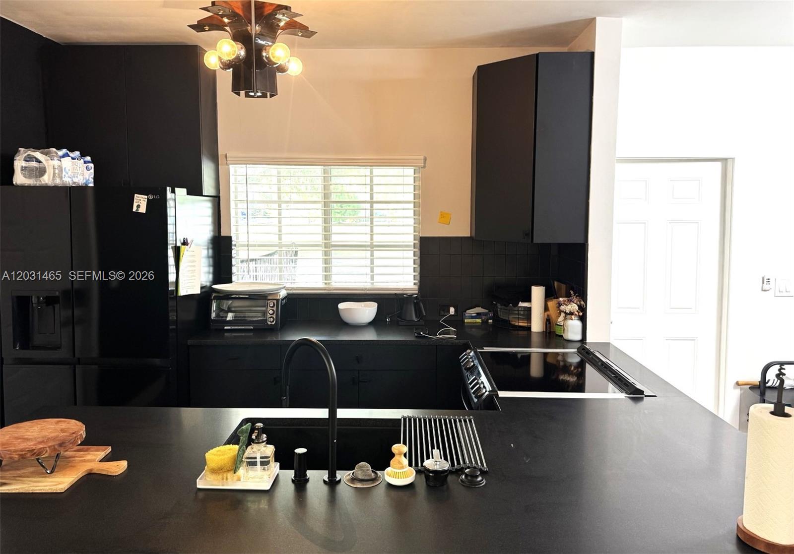 A modern kitchen features black cabinetry, dark countertops, a central island, and a window — 360 NW 19th Ter # 58, Miami FL 33136, MIAMI, FL