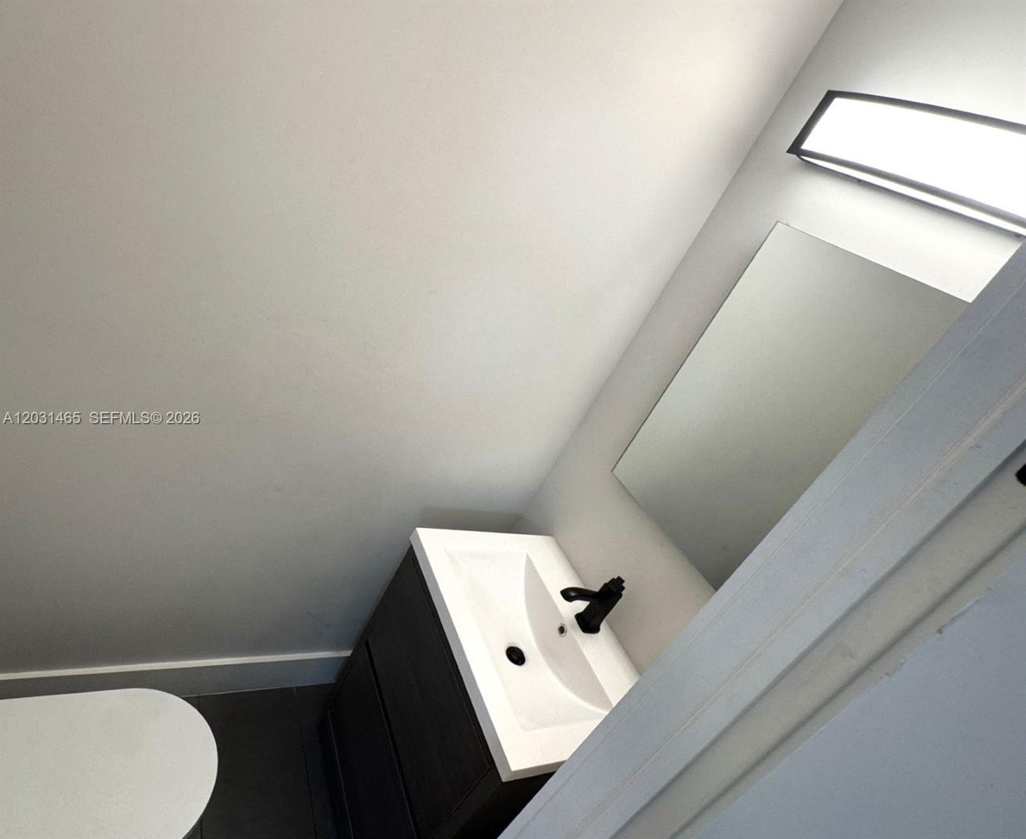 A small bathroom features a dark vanity with a white sink, mirror, and modern lighting — 360 NW 19th Ter # 58, Miami FL 33136, MIAMI, FL