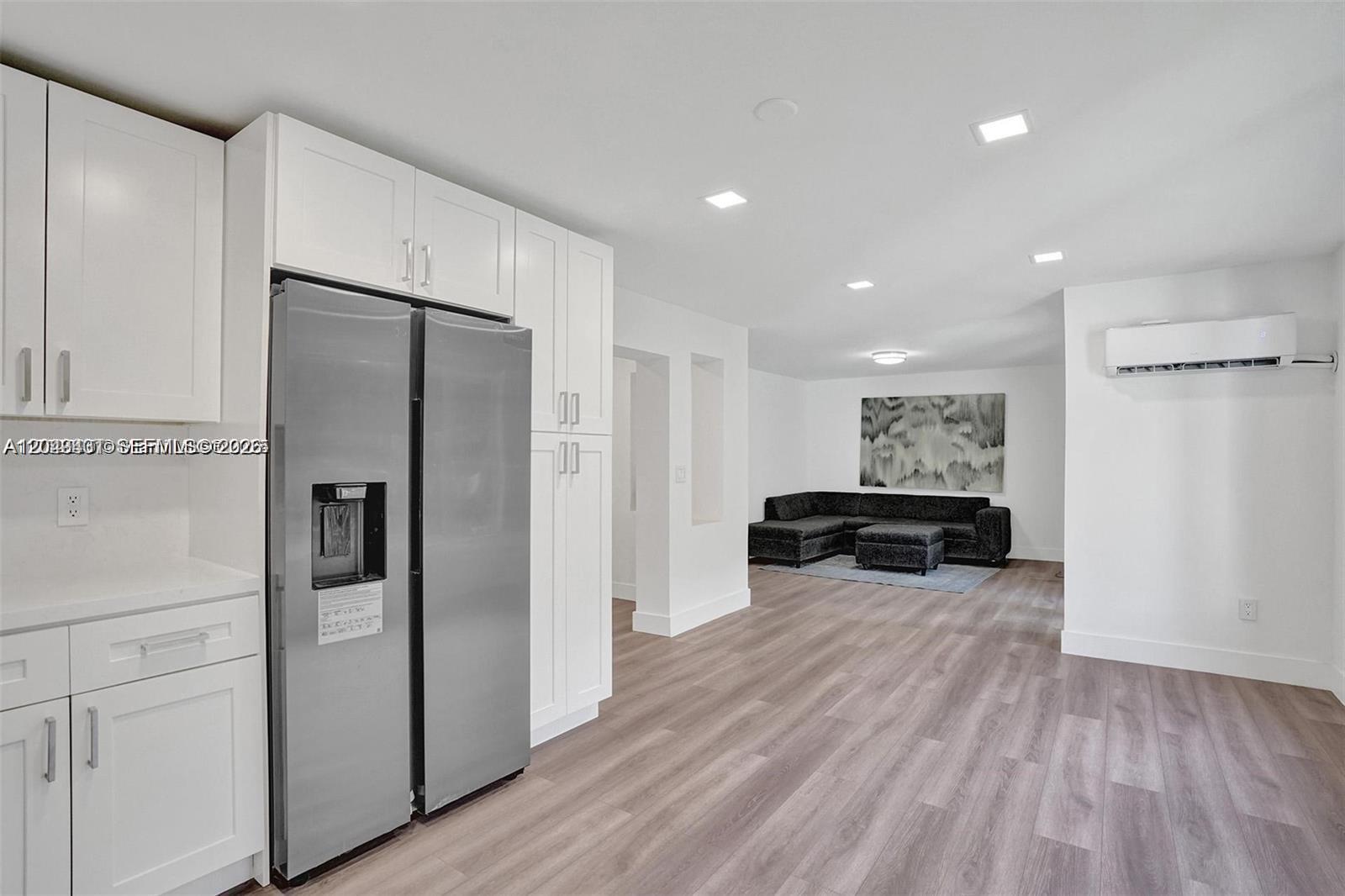 A modern kitchen with white cabinets and stainless steel appliances opens into a living area — 630 NE 52nd Ter, Miami FL 33137, MIAMI, FL