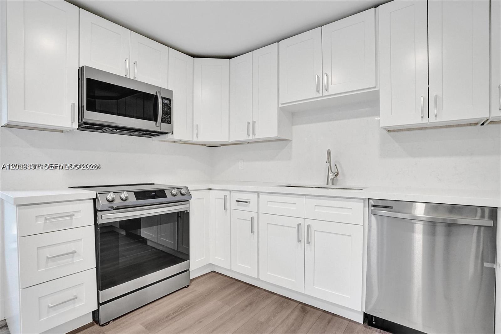 A kitchen features white cabinets, stainless steel appliances, and light wood-look flooring — 630 NE 52nd Ter, Miami FL 33137, MIAMI, FL