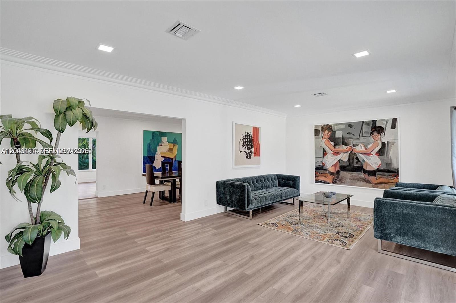 A living room features teal velvet furniture, light wood flooring, and large wall art — 630 NE 52nd Ter, Miami FL 33137, MIAMI, FL