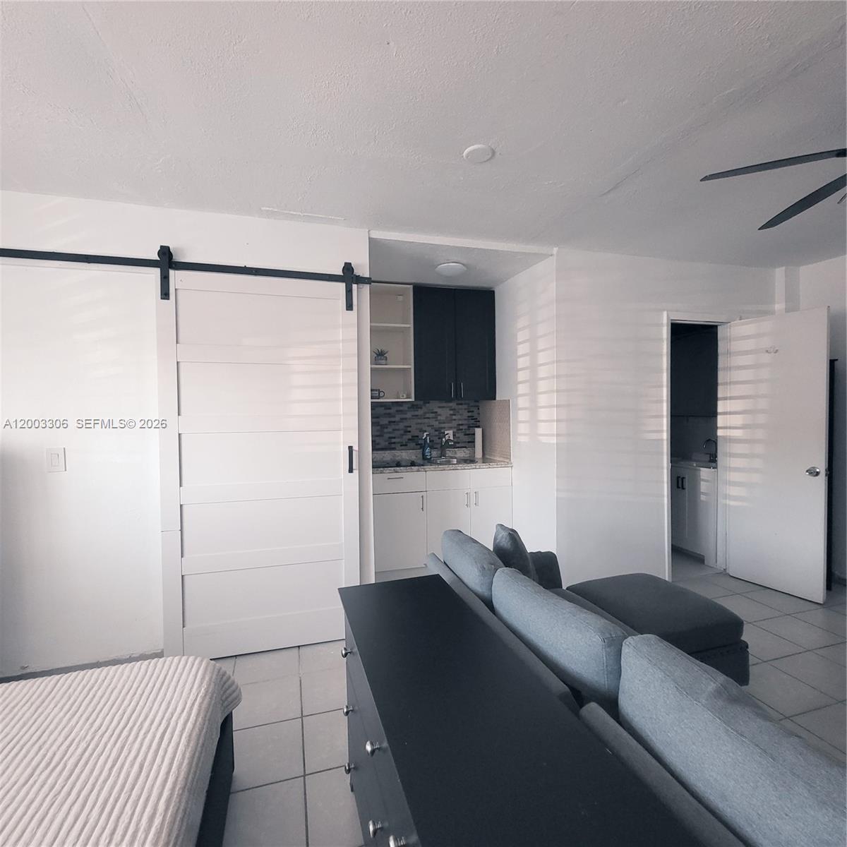 A studio apartment features a kitchenette, a sliding barn door, and a gray sectional sofa — 3405 W Lake Pl # 1, Miramar FL 33023, MIRAMAR, FL