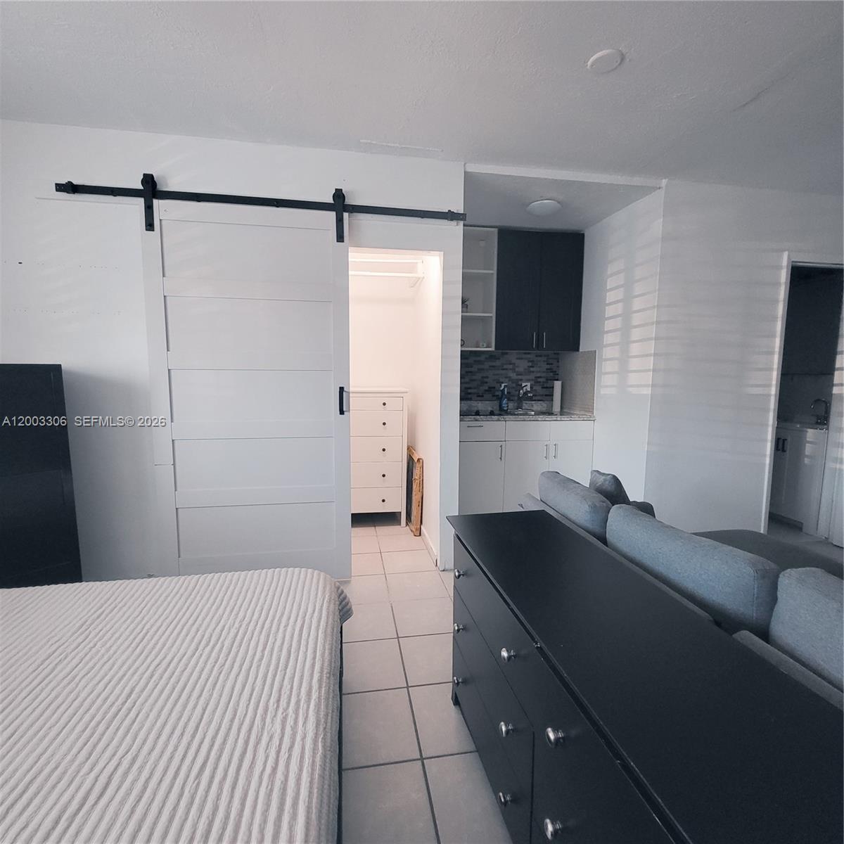 A studio apartment features a bed, a kitchenette, a sliding barn door, and tiled floors — 3405 W Lake Pl # 1, Miramar FL 33023, MIRAMAR, FL
