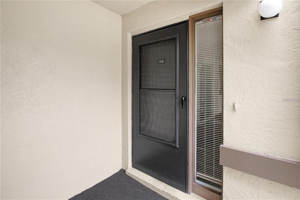 A dark-colored screen door with the number 135 is next to a vertical window — 135 WOODLAKE WYNDE UNIT 135, OLDSMAR, FL