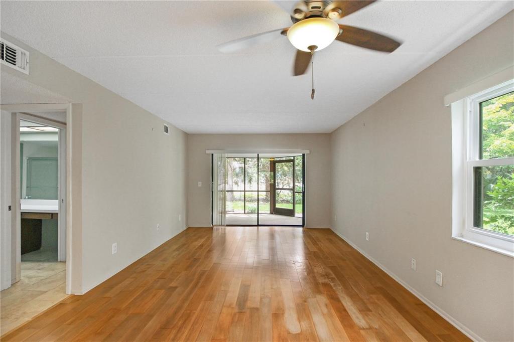 An empty living room features hardwood floors, a ceiling fan, and a sliding glass door — 135 WOODLAKE WYNDE UNIT 135, OLDSMAR, FL