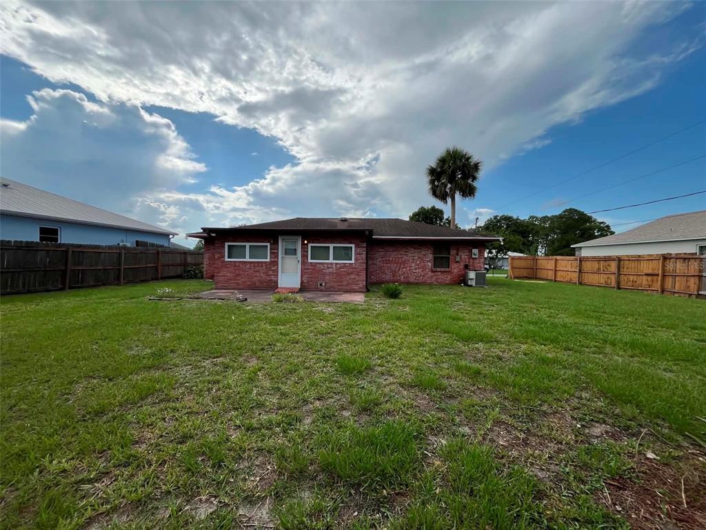 A red brick house exterior features a back door, windows, and a large grassy yard — 688 AIROSO ROAD SE, PALM BAY, FL
