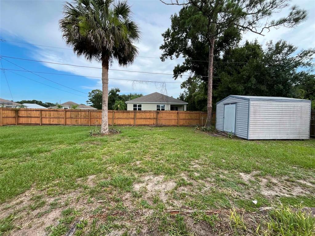 A backyard features a wooden fence, a palm tree, and a small metal storage shed — 688 AIROSO ROAD SE, PALM BAY, FL