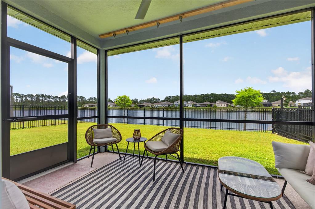 A screened-in patio with outdoor furniture overlooks a grassy lawn, a lake, and distant houses — 222 EAGLE HARBOR WAY, DAYTONA BEACH, FL