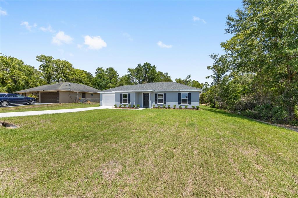 A single-story house with a gray exterior, dark shutters, and a white garage sits on a lawn — 29 OLIVE CIRCLE, OCALA, FL