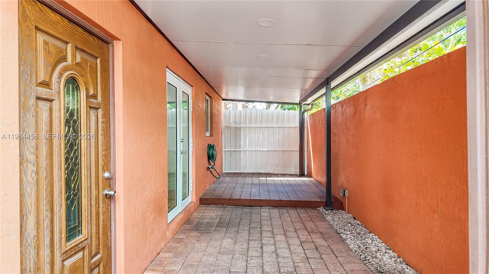 A covered patio features a brick floor, a small wooden deck, and orange stucco walls — 6002 SW 8th St # 3, West Miami FL 33144, WEST MIAMI, FL