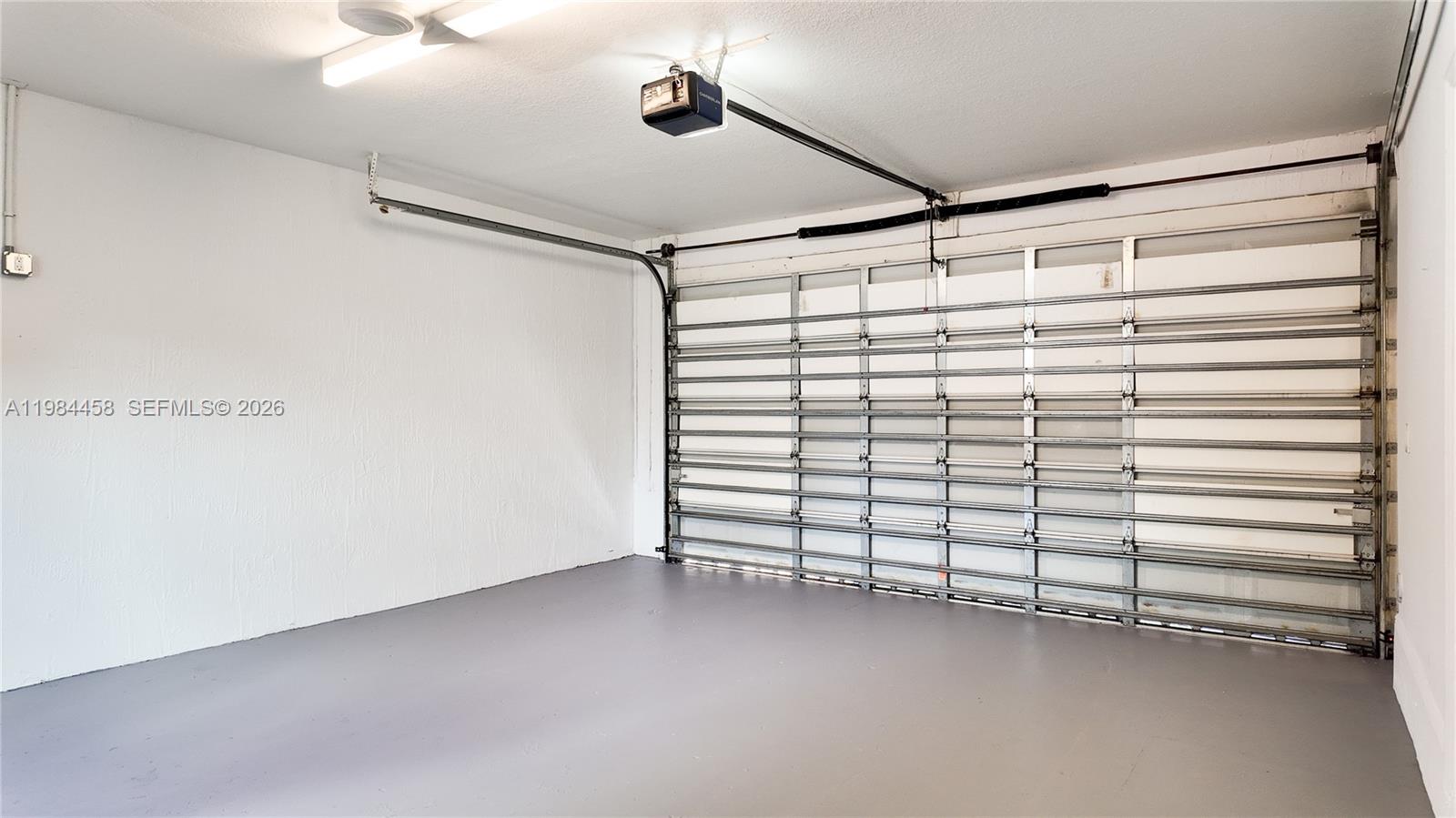 A clean, empty garage features white walls, a gray painted floor, and a metal door — 6002 SW 8th St # 3, West Miami FL 33144, WEST MIAMI, FL
