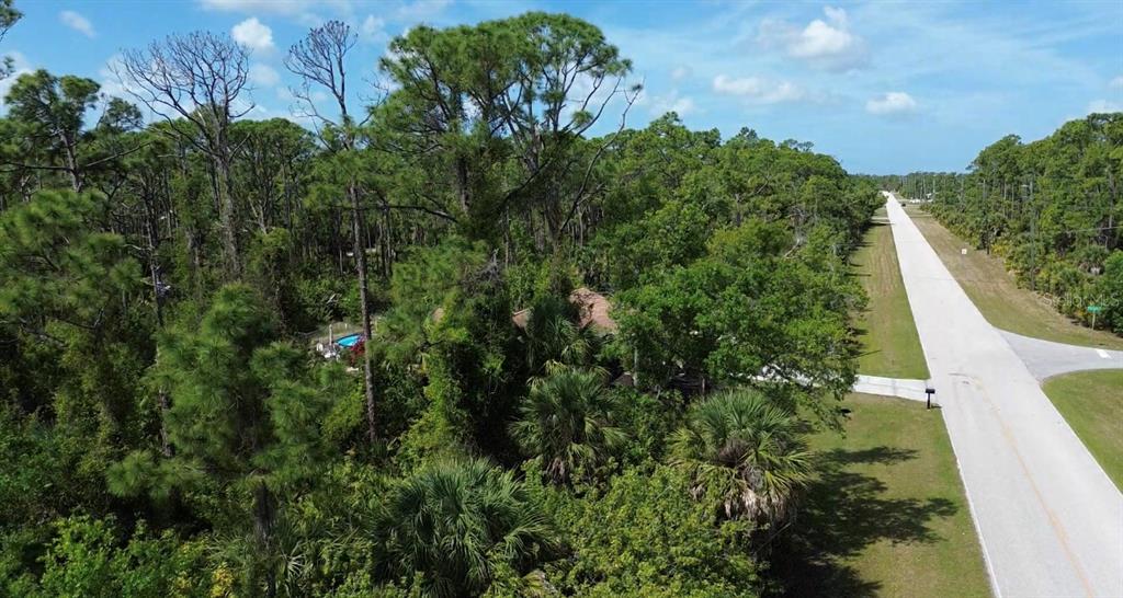 An aerial view shows a house nestled in a wooded lot beside a paved road — 5101 HOPKINS AVENUE, PORT CHARLOTTE, FL