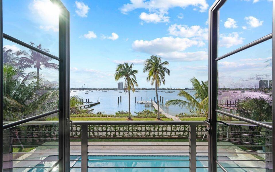 A view of a waterfront pool and bay through open glass balcony doors — 1260 N Lake Way, Palm Beach FL 33480, PALM BEACH, FL