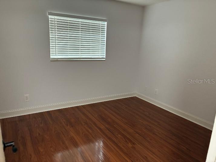 An empty room with hardwood floors, two windows with blinds, and a white entry door — 120 S CHURCH AVENUE UNIT 207, TAMPA, FL