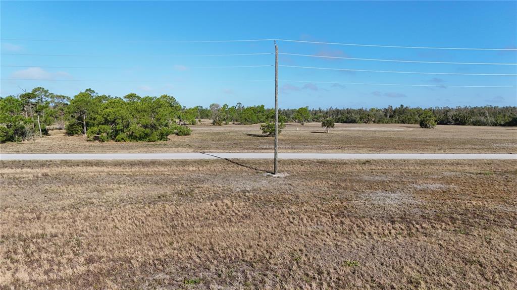An expansive, flat, grassy lot features a paved road and a single utility pole — 14260 BLUEFISH COURT, PLACIDA, FL
