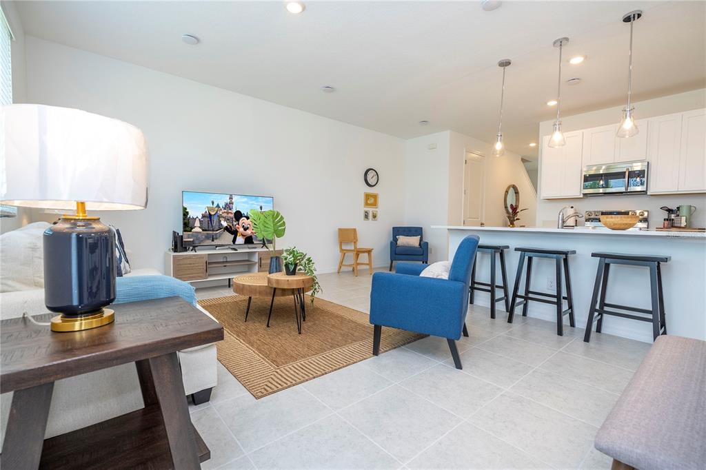 An open-concept living room and kitchen featuring white cabinets, blue armchairs, and tile flooring — 686 LONGBOAT DRIVE, DAVENPORT, FL
